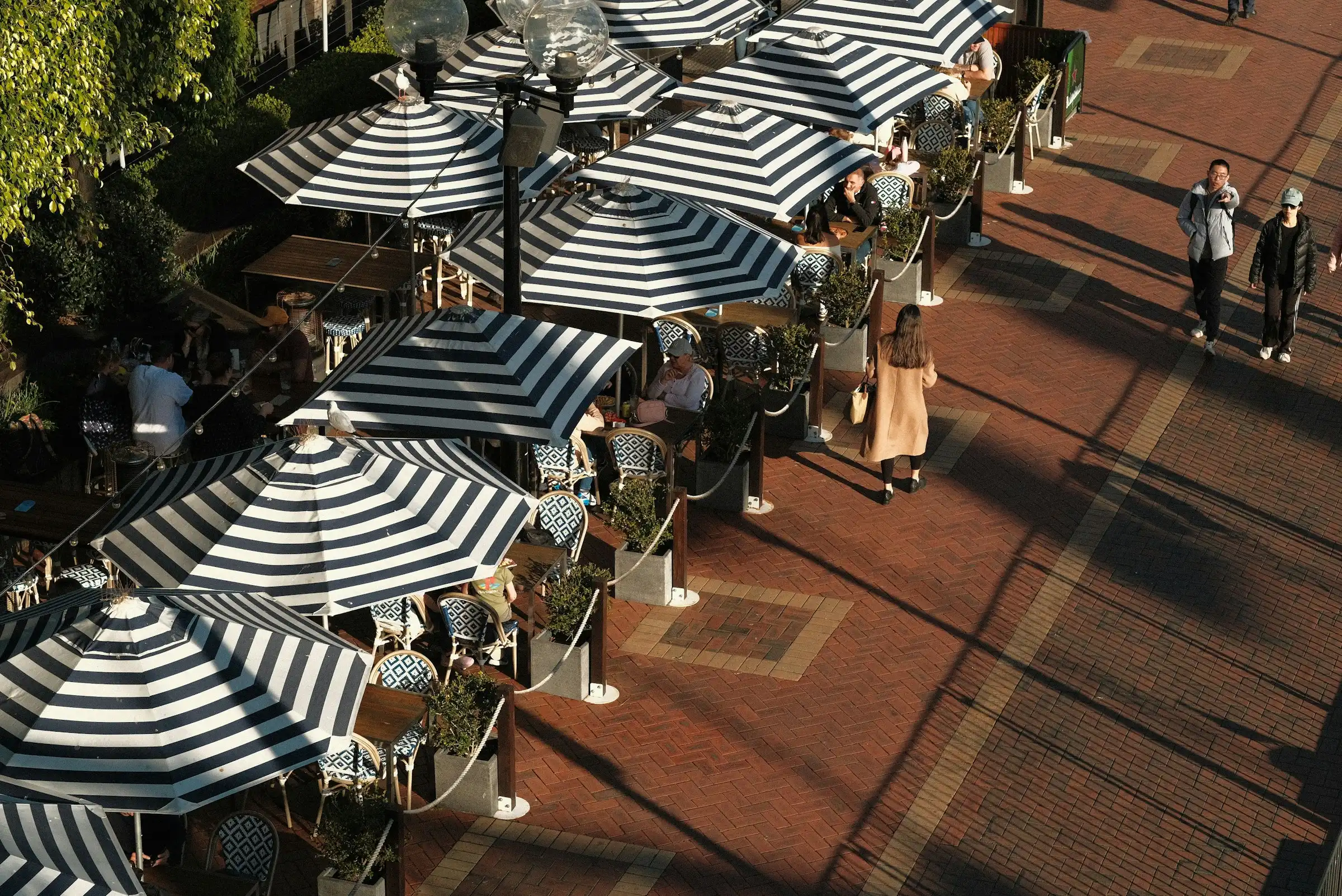 People walking beside outdoor café seating in Darling Harbour, Sydney.